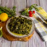 Cretan cuisine. A dish of rare, wild, useful boiled grass "stamnagathi" (Cichorium spinosum), that grows only on Crete with a lemon, close-up on a wooden background (Greece)