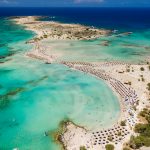 Aerial view of sunshades and umbrellas on a narrow sandy beach surrounded by shallow lagoons (Elafonisso Beach, Crete, Greece)